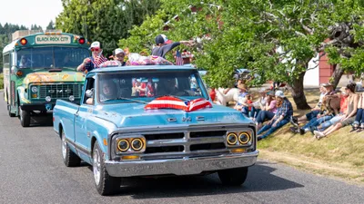 A classic GMC truck draped in an American flag leads a decorated school bus past spectators at the Fourth of July parade in Home, Washington.